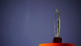 Glass award trophy with laurel wreath rotating on wooden base and orange platform against purple background for achievement recognition winner ceremony celebration