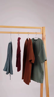 Casual clothing items including pants and shirts appearing one by one on a wooden rack against a clean white background