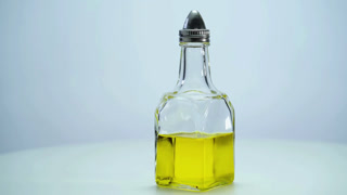A glass bottle filled with bright yellow oil and a metal spout rotating on a white background with clean studio lighting