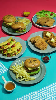 Large assortment of fast food including burgers fries tacos and fried chicken waffles served on plates over a colorful background