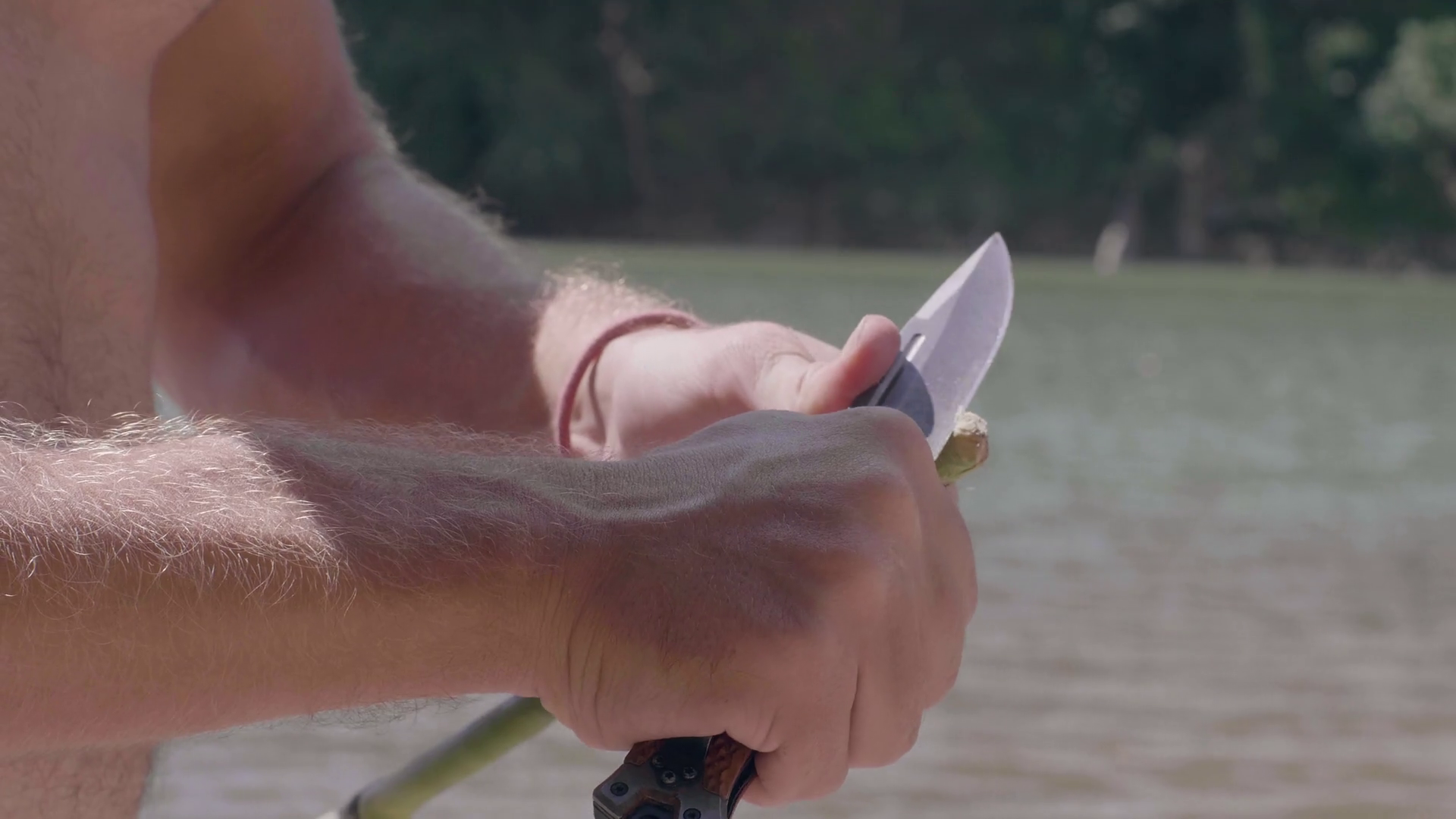 Male hand sharpening wooden stick with survival knife for catching fish