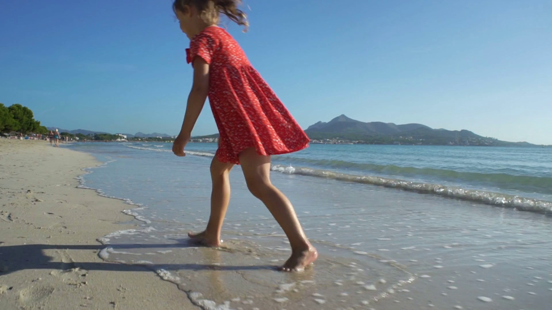 Little girl in bright red dress running on the beach barefoot Stock