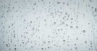 Raindrops on the window dripping down in autumn monsoon. Rainy weather drops knock on window glass. Gray natural background.