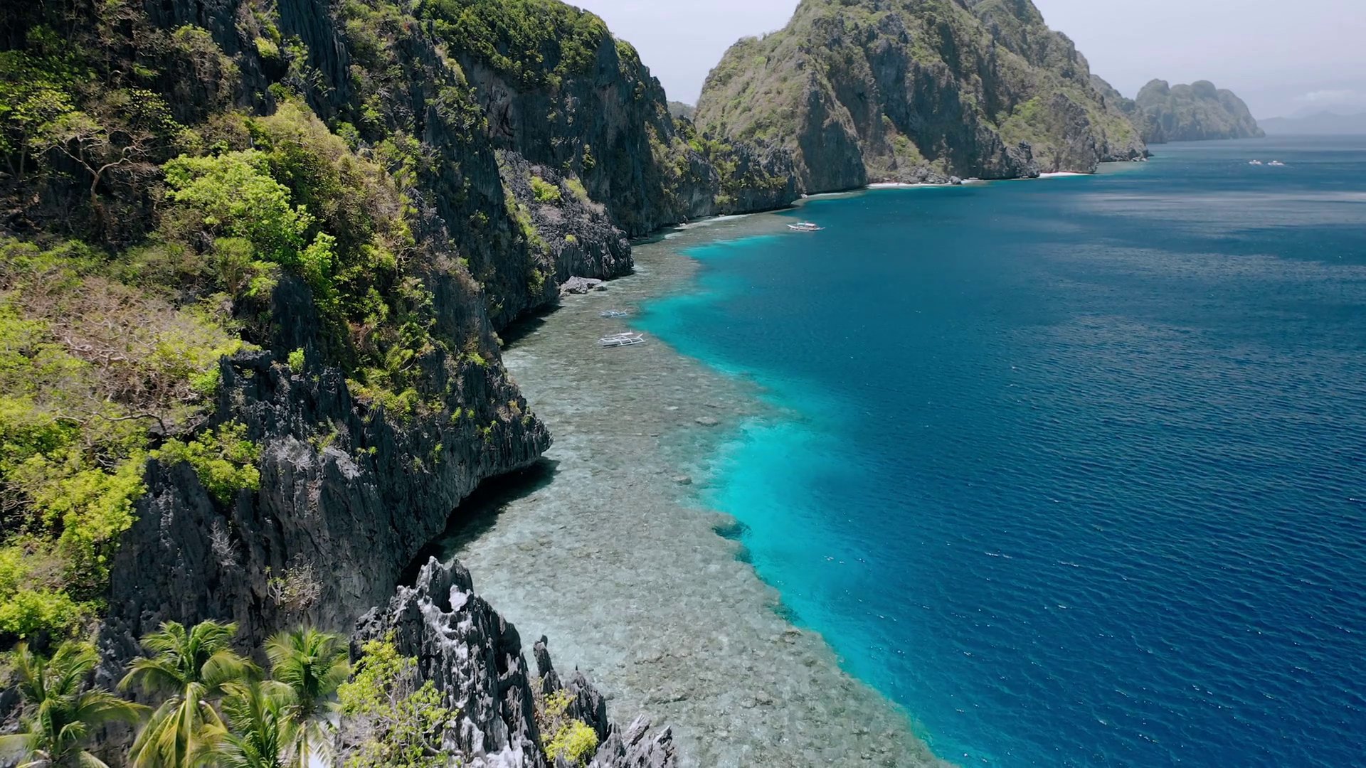 Aerial fly footage over tourist boats, rocky mountains and coral reef near Matinloc shrine. El ...