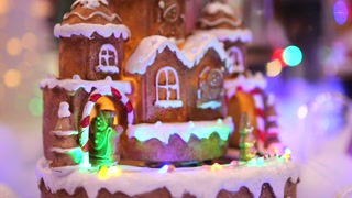 Beautiful gingerbread house with white icing on roof and gingerbread people riding on carousel and on gingerbread sleigh. Cinematic video of