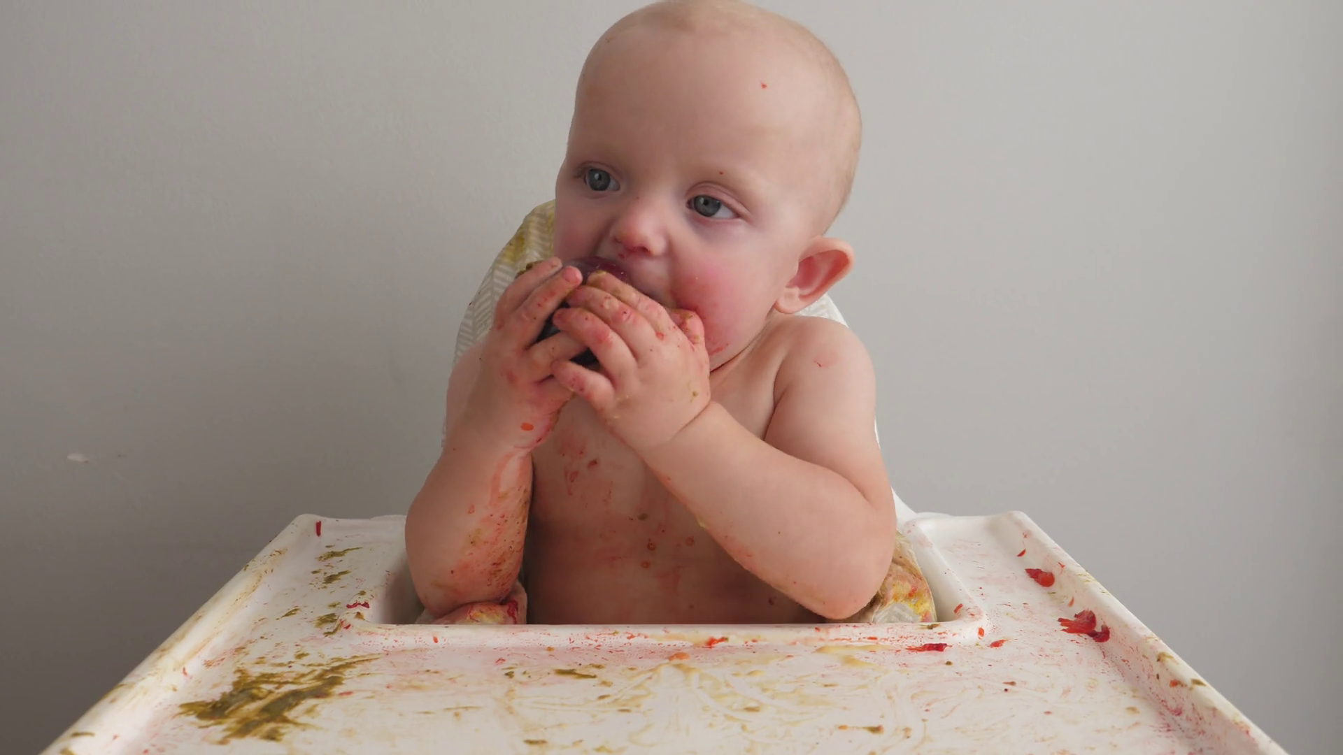 Cute baby girl eating plums and making a mess at home in kitchen. Stock