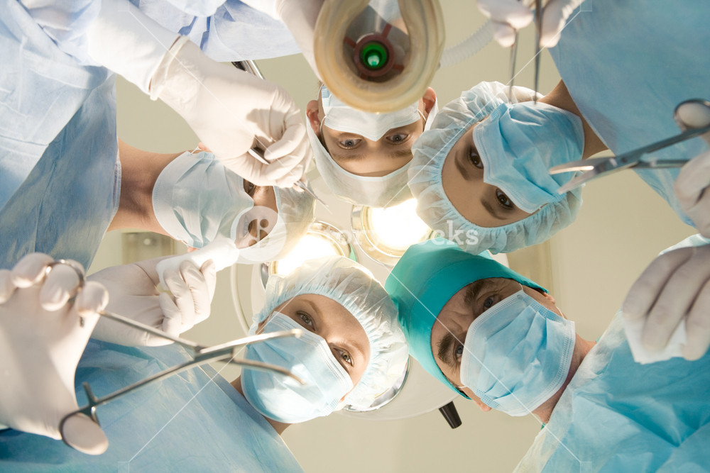 Below view of surgeons holding medical instruments in hands and looking