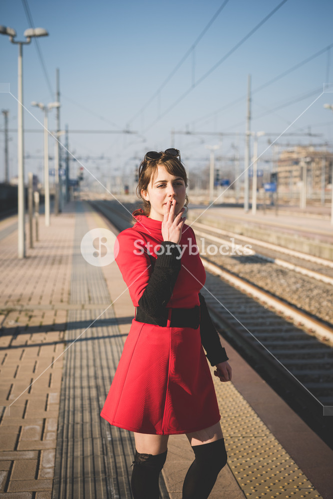 Stylish woman in vintage attire at the station, enjoying a cigarette