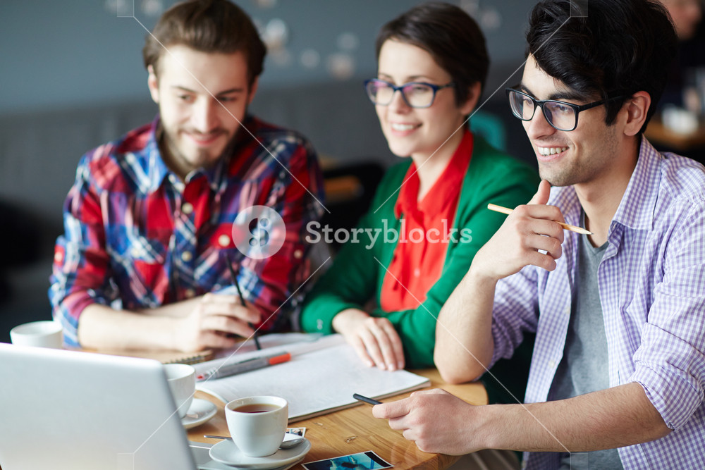 Young professionals collaborating and smiling at work meeting with laptop screen